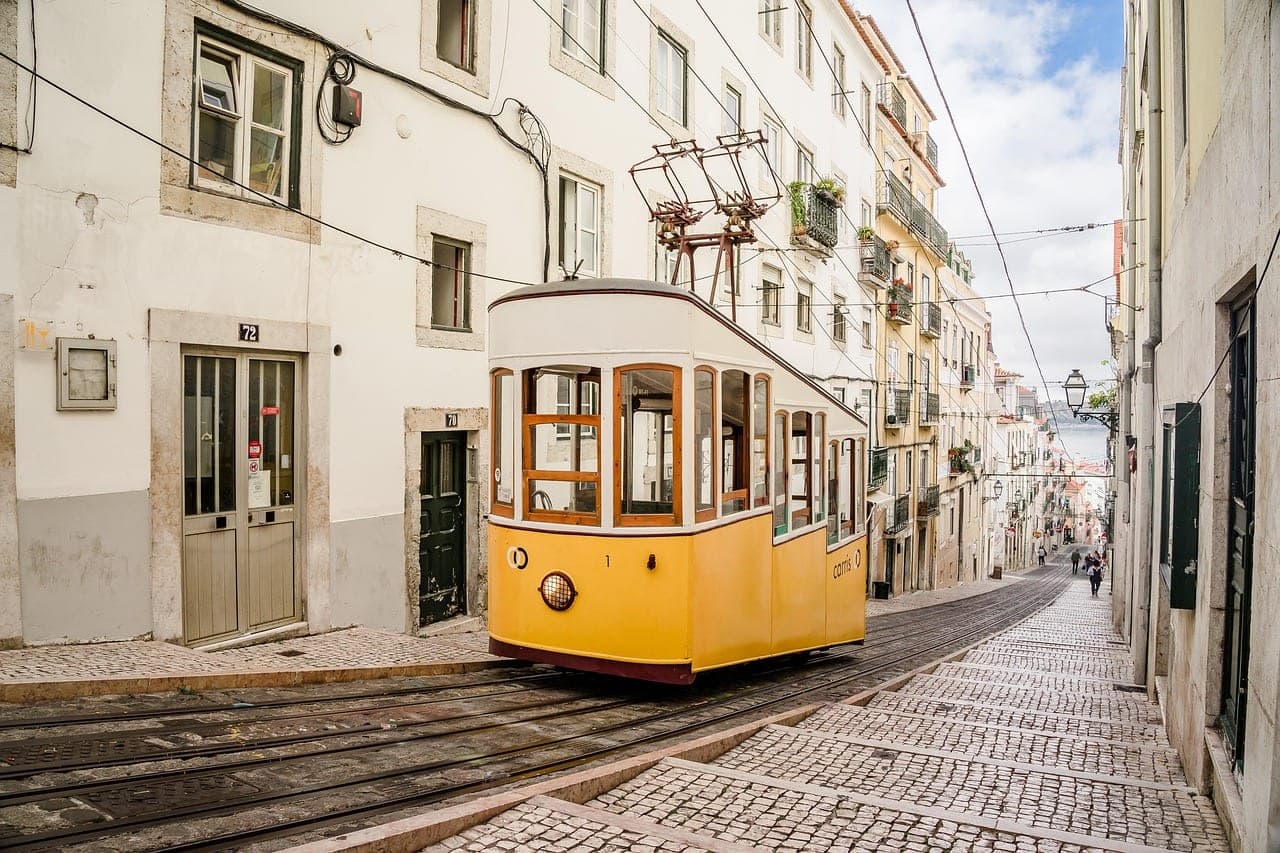 Yellow tram climbing a steep cobbled hillside above red rooftops in Lisbon, Portugal