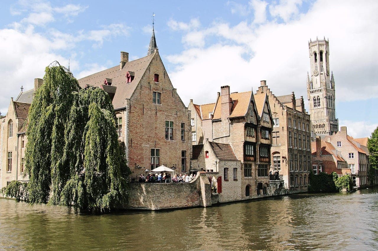 Bruges medieval brick houses and bell tower mirrored in a quiet canal at golden hour