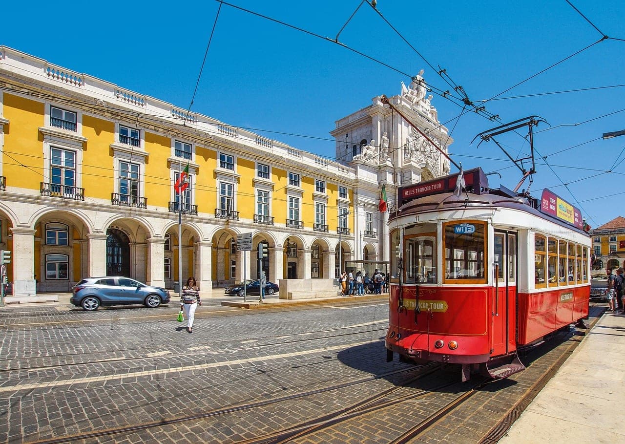 Yellow tram climbing past tiled rooftops above the Tagus river in Lisbon, Portugal