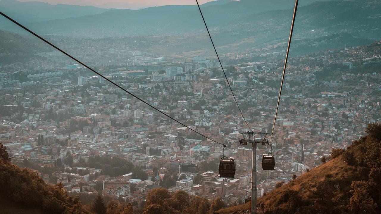 Sarajevo's old town spreading along the Miljacka River with mosque minarets and red-roofed houses ringed by Dinaric peaks